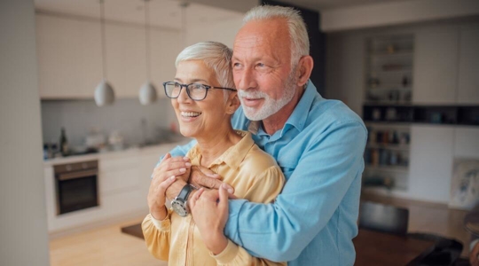 Older couple holding hands on a walk, woman looking back at the camera smiling
